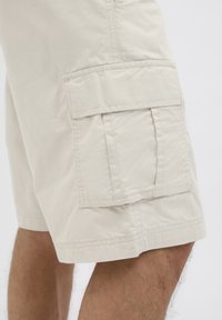 Beige Cargo-Shorts verfügen über eine Seitentasche, gestickte Details, eine leichte Textur und einen geraden Schnitt, der oberhalb des Knies endet.