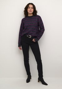 Gehaakte trui met donkere paarse en zwarte strepen, ronde hals, en losse mouwen, gecombineerd met zwarte skinny jeans en enkellaarsjes.