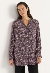 Blumenbluse aus dunklem Stoff mit durchgehender Knopfleiste, kragenlosem Design, langen Ärmeln und einer Mischung aus pinken, weißen und grünen Blumen.