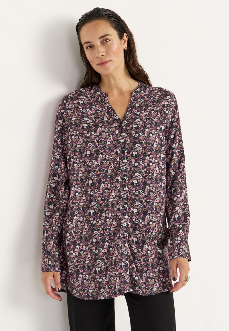 Blumenbluse aus dunklem Stoff mit durchgehender Knopfleiste, kragenlosem Design, langen Ärmeln und einer Mischung aus pinken, weißen und grünen Blumen.