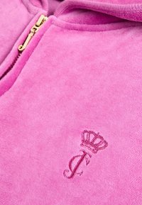 Roza zip-up kapuca iz mehkega materiala z zlatim zadrgo, ki na sprednji strani vsebuje diskretno vezeno krono in logo črke "J".