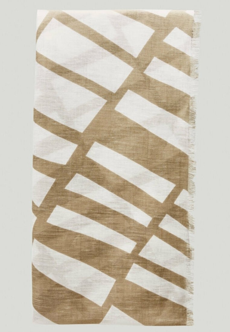 Tissu tissé beige et blanc avec un motif géométrique abstrait et des bords effilochés, étalé à plat sur un fond clair.
