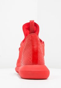 Červená sportovní teniska s hladkým svrškem a texturovanou síťovinou na patě, s gumovou podešví a polstrovaným límcem pro pohodlí.