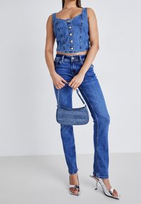 Blå denim avklippt topp med knappstängning och figurnära design, parat med blå denimjeans och en matchande liten handväska. Silverklackar.