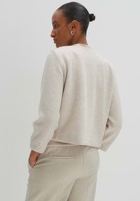 Beiger, kurz geschnittener Pullover aus weichem Stoff mit langen Ärmeln, Rundhalsausschnitt und geripptem Saum, kombiniert mit hellbeigen, maßgeschneiderten Hosen.
