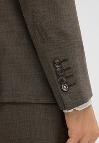 Brązowa, teksturowana tkanina rękawa marynarki garniturowej z czterema czarnymi guzikami i kontrastową dziurką na guzik. Dopasowany krój i strukturalny design.