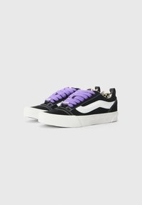 Sneaker neri in suede con lacci viola, una striscia laterale bianca e un motivo testurizzato sulla fodera interna. Suola in gomma spessa.
