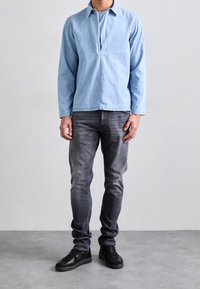 Světle modrá džínsová košile s předním zapínáním a dlouhými rukávy, v kombinaci s tmavě šedými slim džíny a černými teniskami. Jednoduchý design a textury.