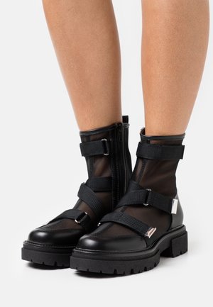 Bottines noires jusqu'à la cheville avec panneaux en maille, sangles contrastantes, éléments en argent, semelles robustes et fermeture éclair latérale.