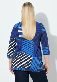 Meer gekleurde pullover met blauwe, marineblauwe en witte geometrische strepen. Driekwartmouwen en zachte, gestructureerde stof.