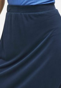 Granatowa spódnica o gładkiej, elastycznej strukturze i elastycznym pasa. Materiał miękko opada, tworząc delikatne fałdy i linie.