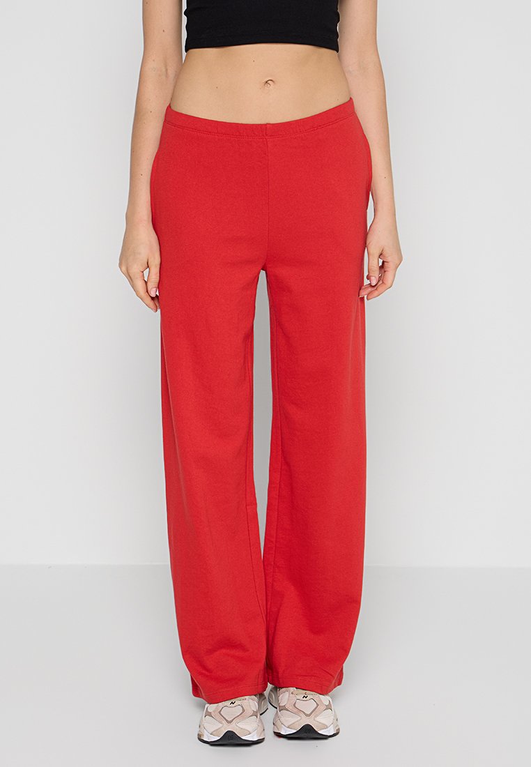 Pantalons larges rouges en tissu doux avec une ceinture élastique. Associés à des baskets de couleur claire avec un motif géométrique.