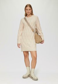 Strickkleid in Creme mit einem strukturierten hexagonalen Muster, kombiniert mit hellbeigen Knöchelboots und einer taupefarbenen Umhängetasche.