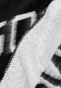 Zwart-wit textiel met een fuzzy textuur, voorzien van gedurfde grafische patronen en een zigzag gestikte rand voor extra duurzaamheid.