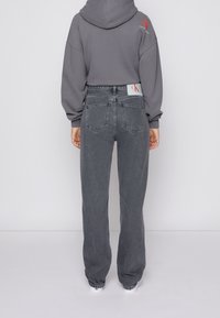 Sudadera gris recortada con capucha y jeans gris de cintura alta. La sudadera presenta un logo; los jeans tienen cinco bolsillos y un acabado texturizado.