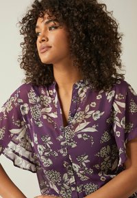 Lila, durchsichtige Bluse mit Floralprint, kurzen, schwingenden Ärmeln und einer durchgehenden Knopfleiste mit subtilen Knöpfen sowie einem lässigen Schnitt.