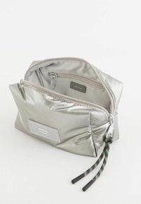 Srebrna nylonowa torba z teksturowanym, błyszczącym wykończeniem oraz kolorowym, plecionym sznureczkiem; posiada główną komorę zamykaną na zamek błyskawiczny i metkę z etykietą.