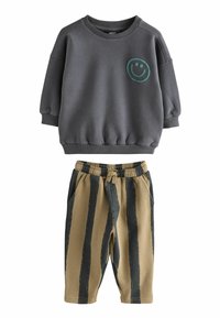 Felpa a maniche lunghe grigio ardesia con faccina sorridente verde e pantaloni beige con ampie strisce verticali nere e cintura elastica.