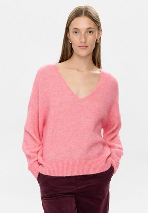 Pulover roz moale cu decolteu în V, cu mâneci lungi și tiv cu nervuri, purtat peste pantaloni de un burgund închis. Materialul pare pufos, având o textură confortabilă.