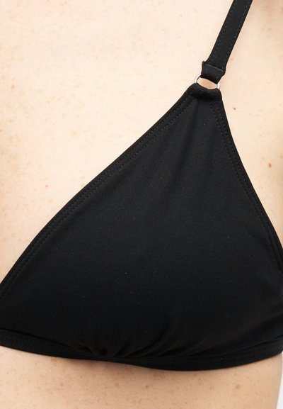Κοντινό πλάνο μιας μαύρης μπικίνι κορυφής σε σχήμα τρίγωνου με ρυθμιζόμενο λουρί σε ανοιχτόχρωμο δέρμα με φακίδες.