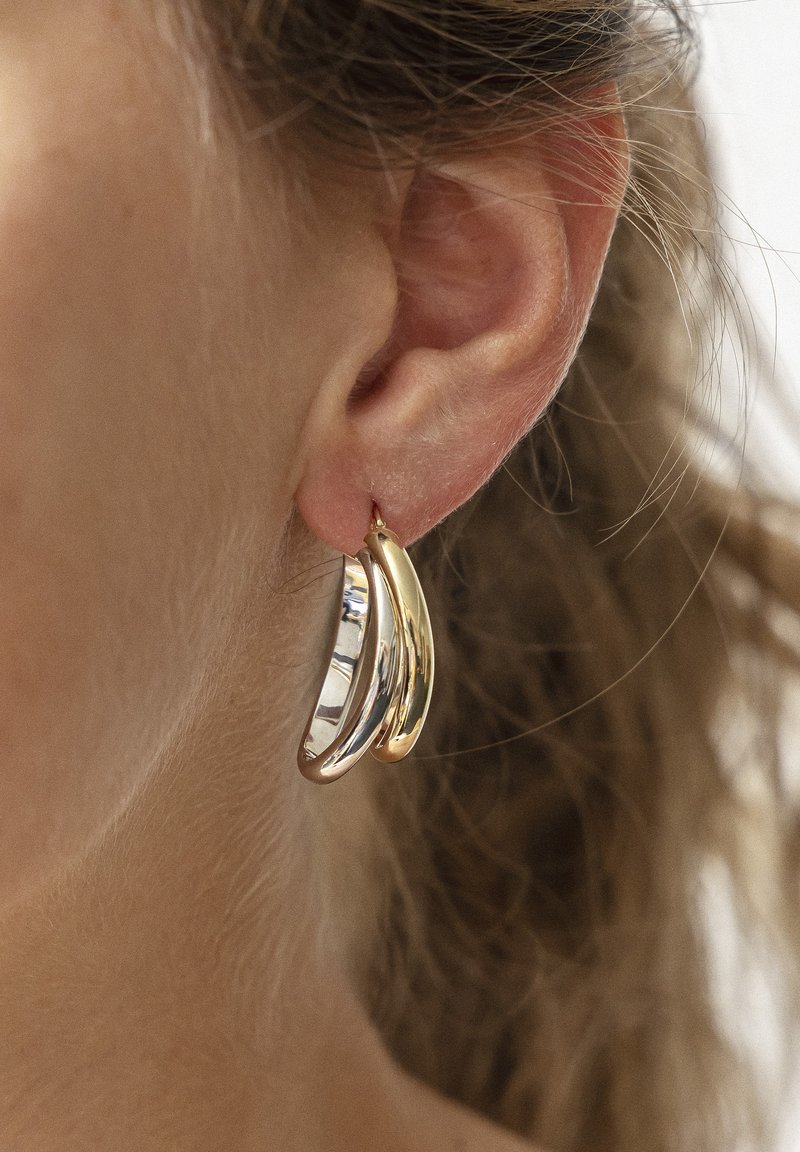 Orecchini a cerchio in oro e argento con una forma curva, caratterizzati da una finitura lucida e un design a strati che crea una texture visiva dinamica.