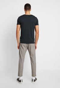 Black short-sleeve t-shirt paired with gray plaid trousers, featuring a slim fit and contrasting white socks and dark sneakers.