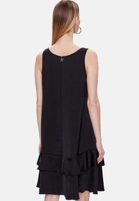 Vestido negro sin mangas con un dobladillo de volantes en capas, textura suave y un pequeño acento de estrella en la parte posterior del escote.