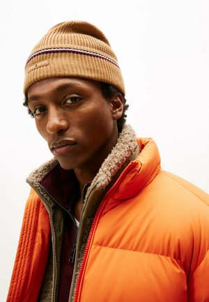 Knit hat in tan with multicolored striped accent. Orange puffer jacket with a fleece-lined collar, layered over a maroon inner jacket.