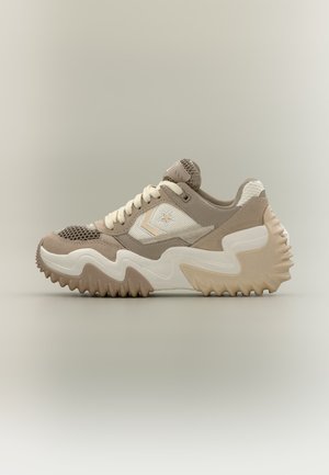 Beżowo-biały sportowy sneaker z grubą, falistą podeszwą i fakturowaną siateczką, sznurówkami oraz logo gwiazdy z boku, pokazany z profilu na jednolitym tle.