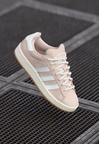 Svijetlopinkaste suede tenisice s bijelim prugama i detaljima, guste bijele vezice i bež gumeni potplat. Sadrži podstavljeni ovratnik za udobnost.