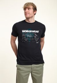 Černé tričko s bílým grafickým textem a jednoduchým výkresem dodávky. Design zahrnuje prvky "WORKERWEAR" a "JUNKERS YARD".