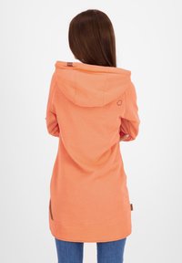 Sweat à capuche à manches longues en corail, avec une capuche, des fentes sur les côtés et un tissu texturé. Comprend un petit logo sur le dos.