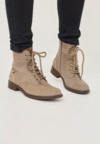 Stivaletti alla caviglia in suede beige con punta arrotondata, chiusura a lacci, occhielli in metallo e zip laterale. Tacco basso a blocco e suola texturizzata.