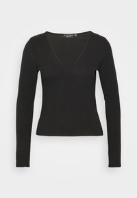 Top preto de manga longa com um formato justo, decote em V, textura suave e tecido canelado. Etiqueta visível no decote.
