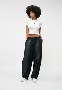 Λευκό κοντό μπλουζάκι με μαύρο λογότυπο, συνδυασμένο με χαλαρές μαύρες φόρμες που διαθέτουν ελαστική μέση και πλάγιες τσέπες. Λευκά υποδήματα.