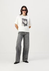 Tricou alb supradimensionat cu un grafic alb-negru, asortat cu blugi gri cu talie înaltă și picior larg și cizme negre cu toc.