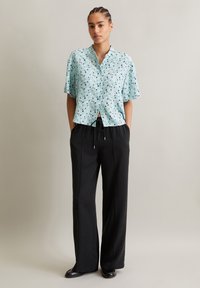 Light blue, short-sleeved shirt with a floral print; paired with loose black trousers featuring side pockets and a drawstring waistband.