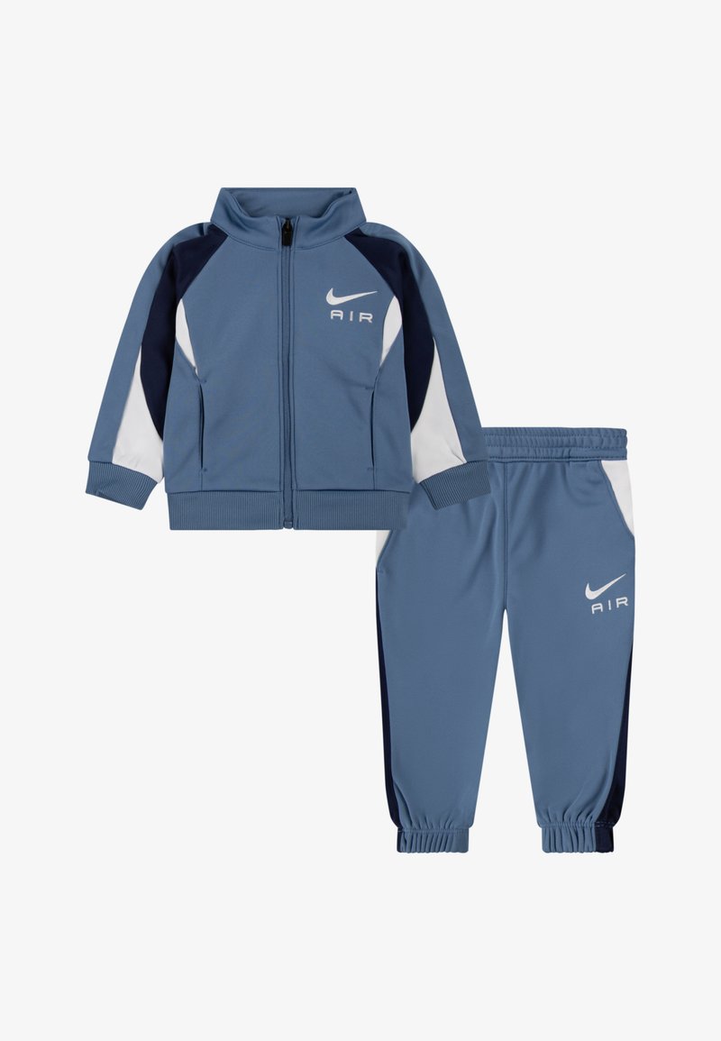 Sininen Nike Air lasten urheiluasu, jossa on vetoketjullinen takki ja joustovyötäröiset housut, joissa on valkoisia ja tummansinisiä värilohkoja.