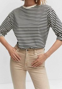 Top de rayas en blanco y negro de manga larga combinado con unos vaqueros de tiro alto en beige claro. La tela parece suave y con un ajuste relajado.