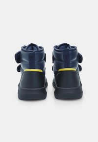 Granatowe lity sportowe buty z wyściełanym wsparciem kostki, paskami na rzepy i teksturowaną gumową podeszwą. Żółty akcent na pięcie.