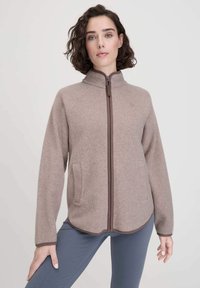 Hellbraune Fleecejacke mit hohem Kragen, Frontreißverschluss und Seitentaschen. Verfügt über Raglanärmel und einen geschwungenen Saum mit braunen Akzenten.