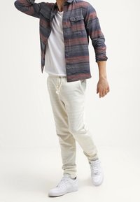 Avslappnad outfit med en marinblå och rostfärgad randig skjorta med knappar, vit t-shirt, ljuskrämfärgade joggers och vita sneakers.