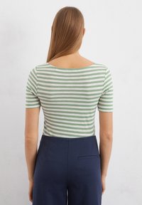 Grün-weißer gestreifter Kurzarm-Oberteil mit weitem Halsausschnitt, kombiniert mit dunkelblauen Hosen mit einer Gesäßtasche.