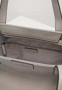 Intérieur d'un sac à main en cuir gris avec une poche zippée et une étiquette de marque. Texture lisse, forme structurée, doubles poignées pour le transport.