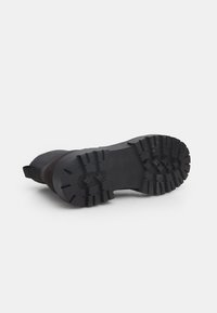Suela de goma negra con un patrón de tracción resistente. La sección superior presenta una tela texturizada para mayor durabilidad. Incluye talón reforzado y una pestaña para tirar.