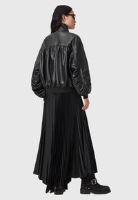 Černá kožená bomber bunda se staženou zadní částí, kombinovaná s dlouhou plisovanou černou sukní a masivními černými bojovými botami.