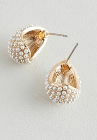 Orecchini a cerchio in tono dorato adornati con piccole perle bianche, con un design aperto texture e ganci in metallo per indossarli in tutta sicurezza.
