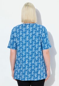 Top azul de manga corta con un patrón paisley blanco, escote redondo y un corte holgado. Se muestra desde la parte de atrás con un dobladillo curvado.