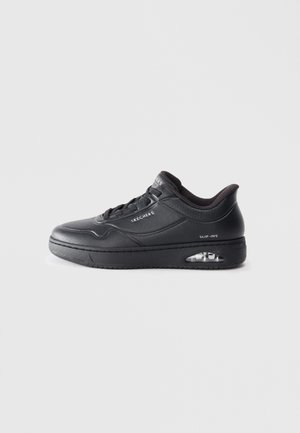 Black sneaker with a textured leather upper, round toe, lace-up design, and a visible air cushioning unit in the sole. Features branding on the side.