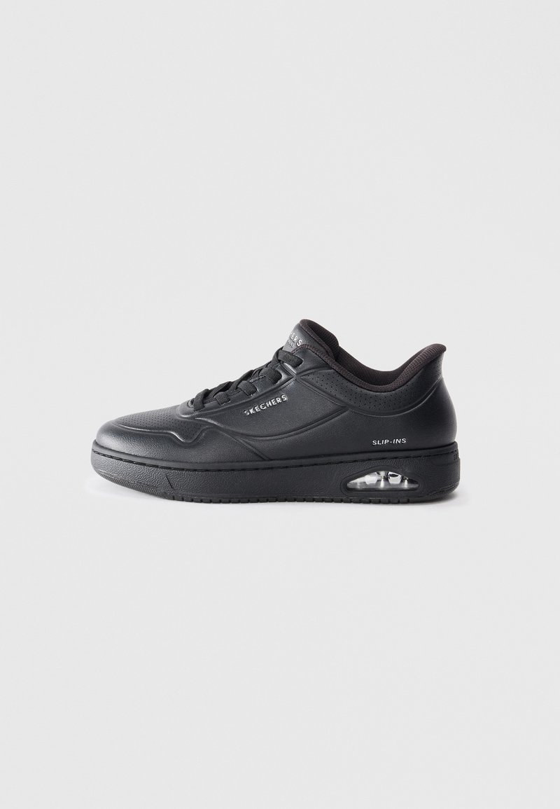 Black sneaker with a textured leather upper, round toe, lace-up design, and a visible air cushioning unit in the sole. Features branding on the side.